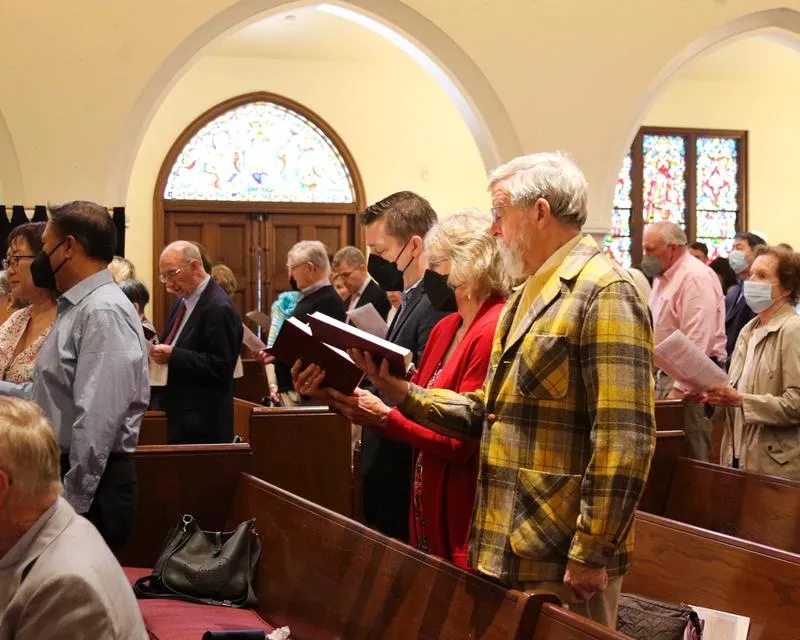 Masked and unmasked people single from hymnals while standing in pews.
