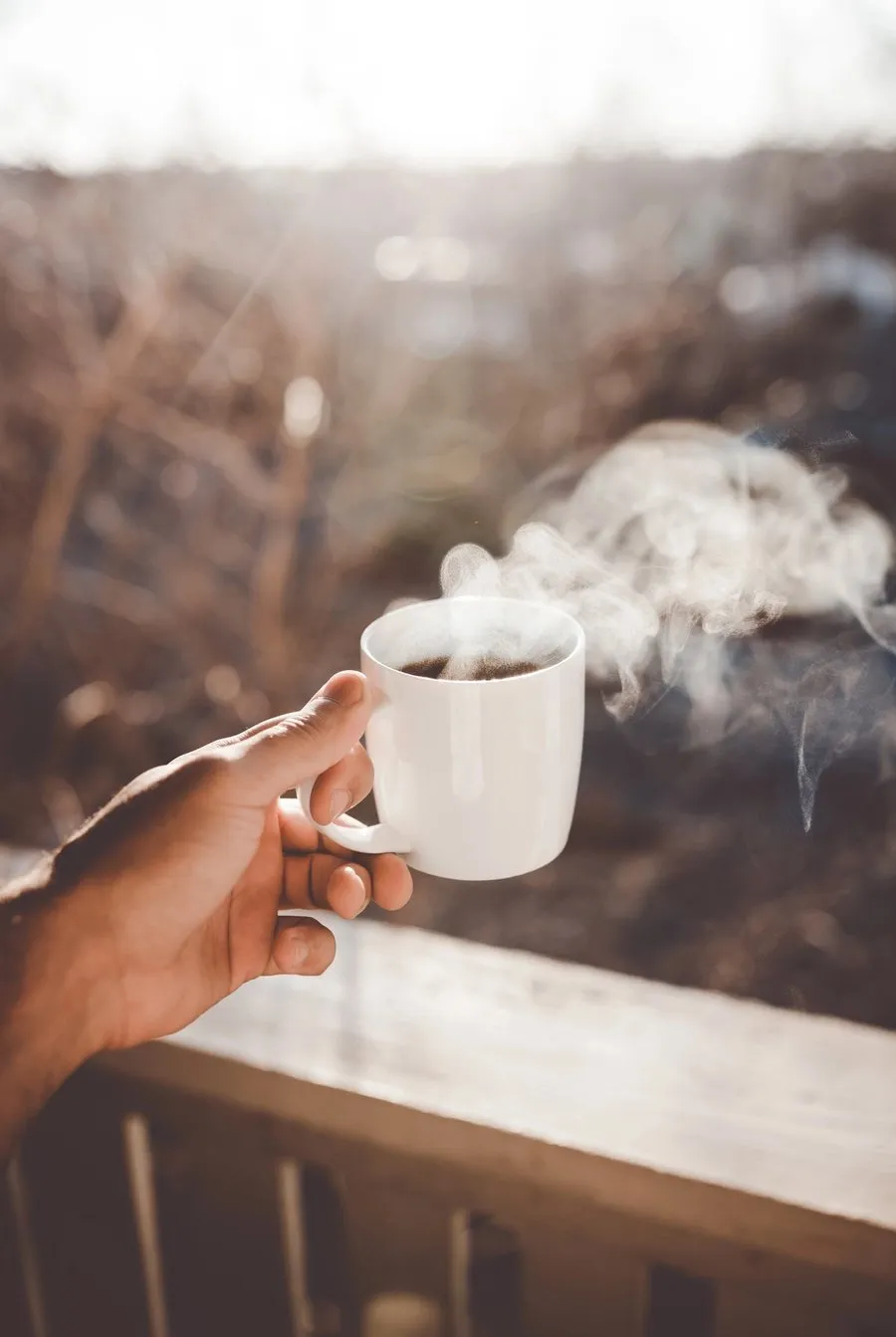 A white ceramic mug filled with steaming coffee in morning light.