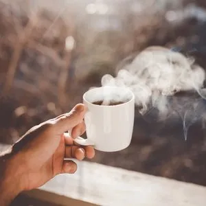 A white ceramic mug filled with steaming coffee in morning light.
