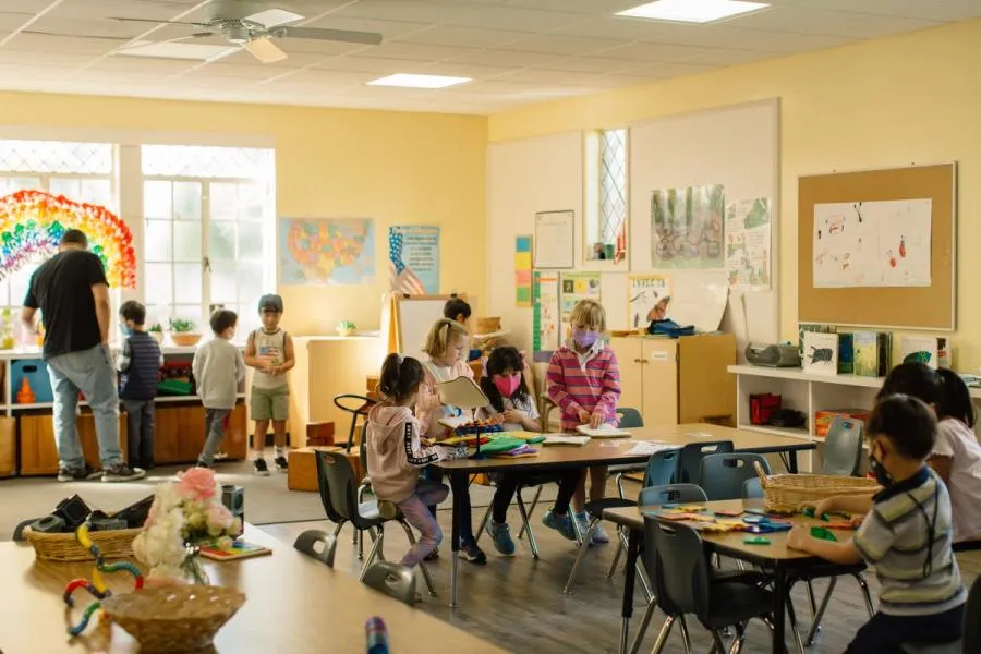 Children work on different tactile projects at activity tables in a classroom.