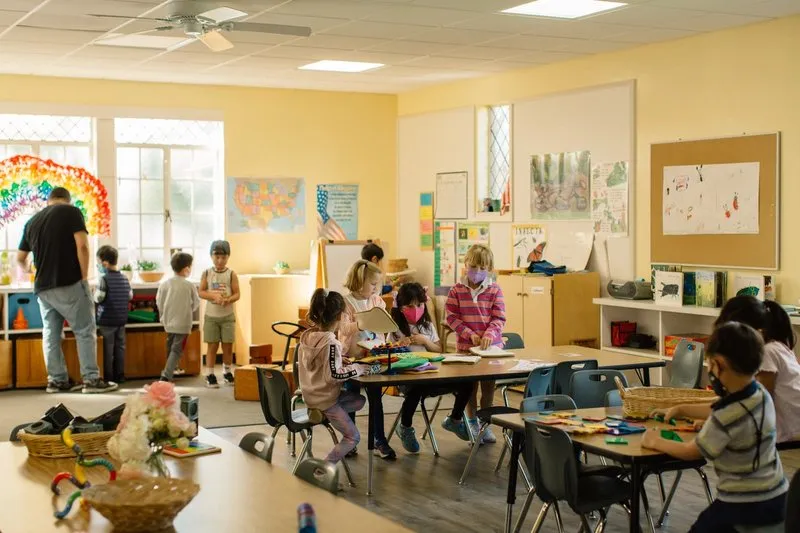 Children work on different tactile projects at activity tables in a classroom.