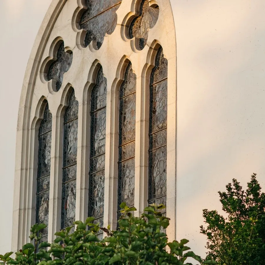 Exterior of main stained glass window foregrounded by greens.