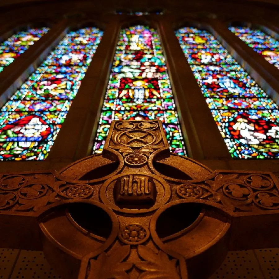 looking up at a carved stone cross that stands below five stained glass windows.