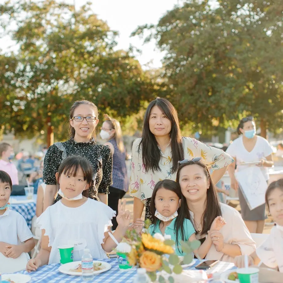 Three adult women and four children pose at a gingham covered table in the late afternoon in the parking lot of SMCC.