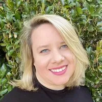 Hailey Horne, Administrative Assistant for Development & Communications. A smiling woman with blonde hair in front of green foliage.