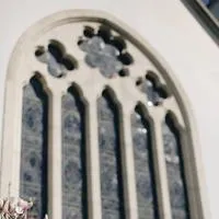 Slightly blurred exterior of church stained glass window with pink flowers in the foreground.