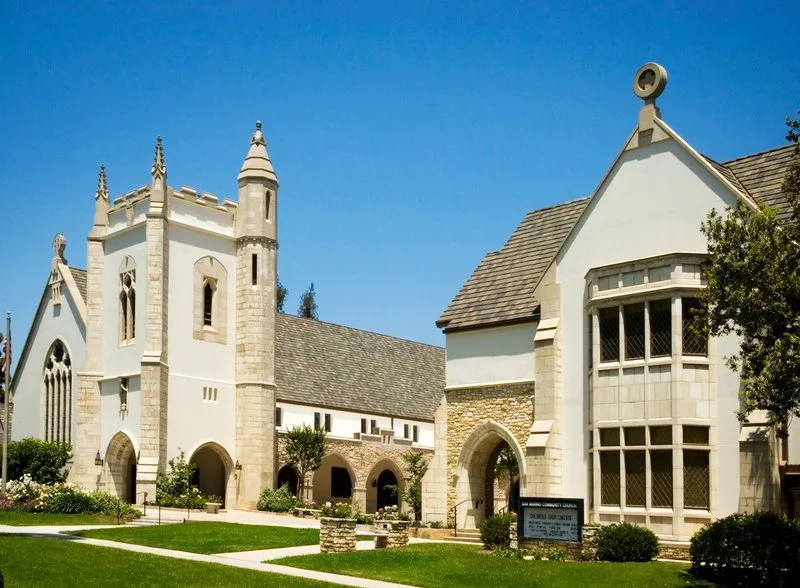 Front exterior of church showing a green lawn and white stone architecture of church.